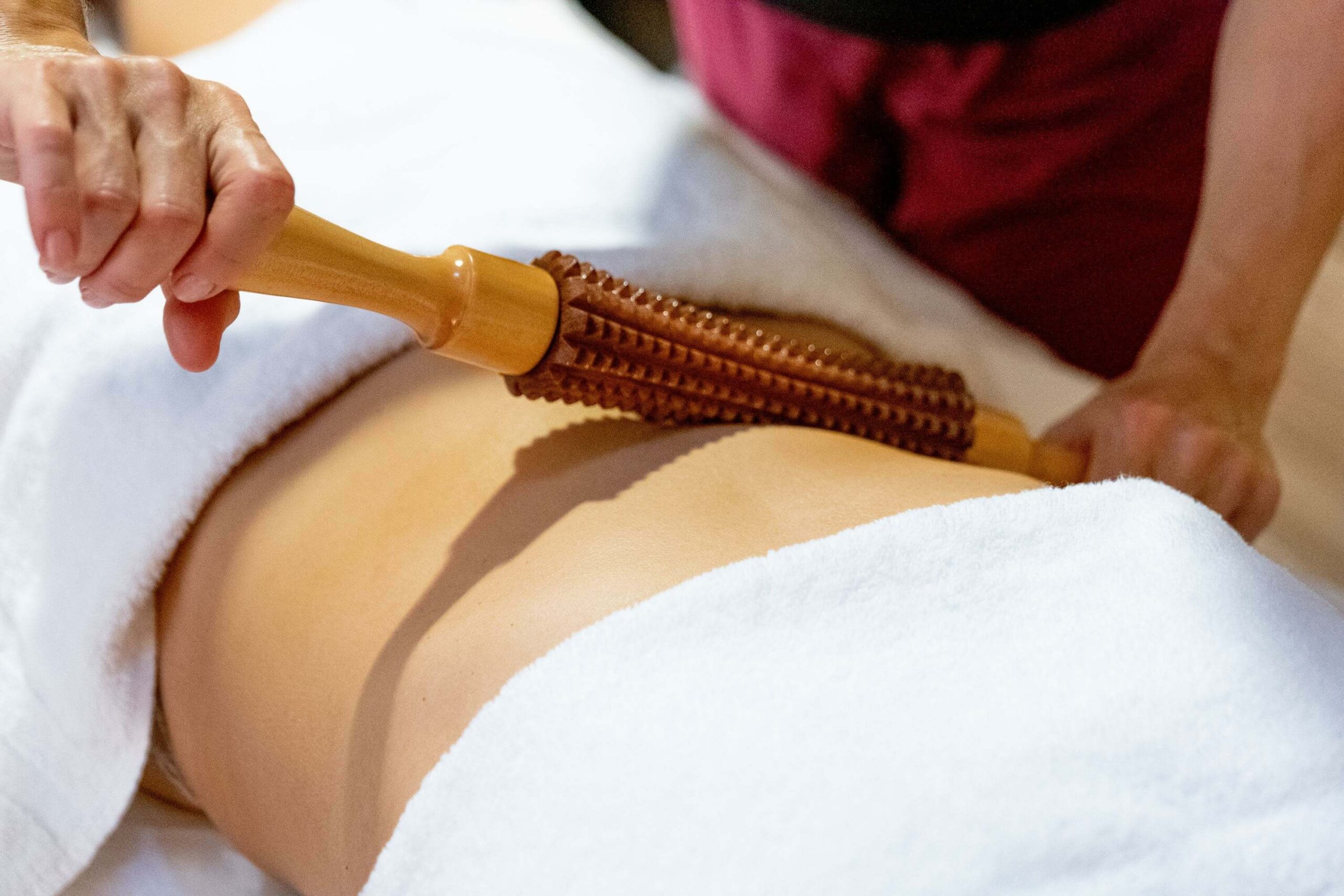 Woman using a wood roller to perform wood therapy to break up fat tissue on lower back